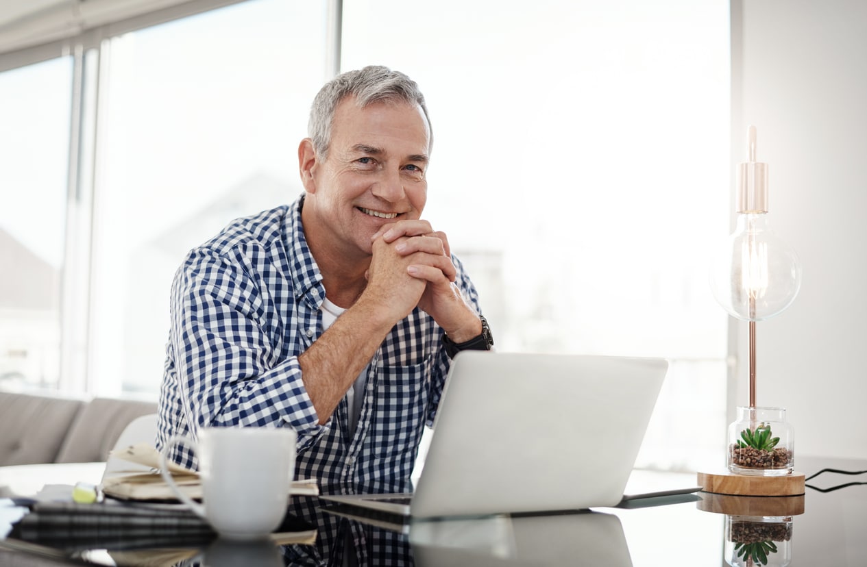 a man sits at a table with his hands folded in front of a laptop