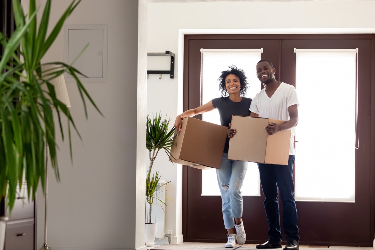 Happy african couple holding big boxes entering modern house