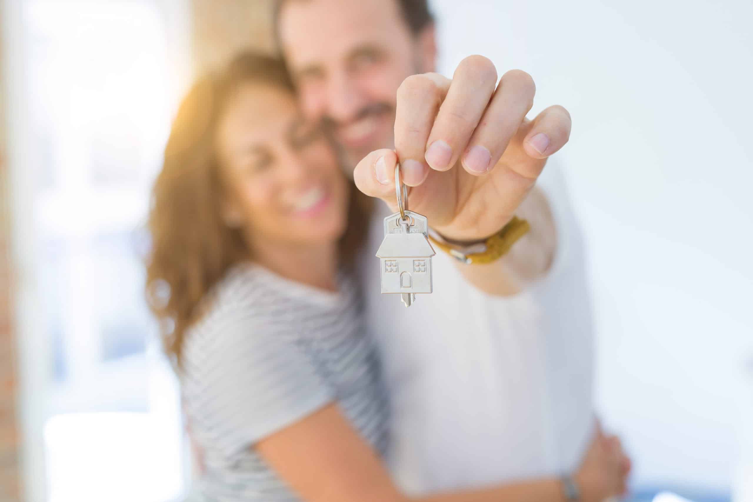 a man is holding a house key in front of a woman